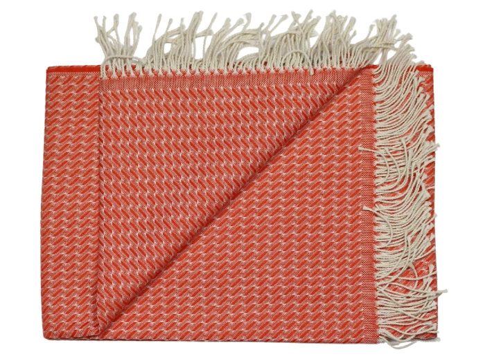 Et foldet orange og hvidt vævet tæppe med et chevronmønster og frynsede kanter på den ene side.