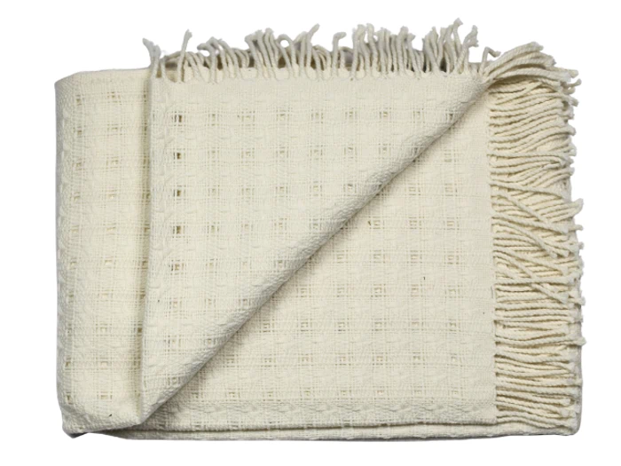 Et foldet cremefarvet vævet tæppe med frynsede kanter og et diskret ternet mønster.