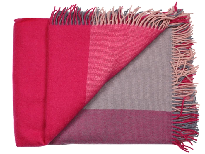 Et foldet uldtæppe med et ternet mønster i røde, rosa og grå nuancer og med frynsede kanter.