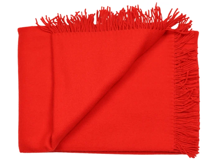 Et knaldrødt, frynset tæppe, der er pænt foldet med det ene hjørne vendt om, så man kan se den bløde tekstur og kvasterne langs kanterne.