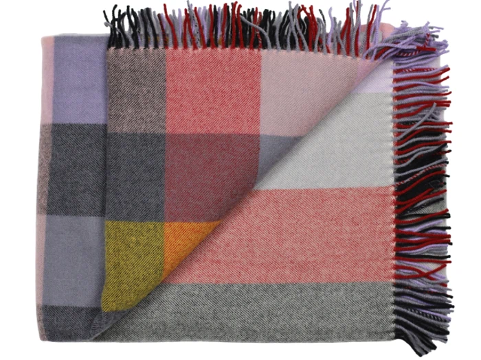 Et foldet uldtæppe med et stort ternet mønster i nuancer af rosa, grå, gul, lilla og rød, med flerfarvede frynser på kanterne.
