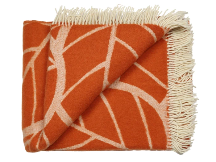 Et orange og cremefarvet tæppe med frynser er foldet og har et geometrisk cremefarvet stregmønster på den orange baggrund.