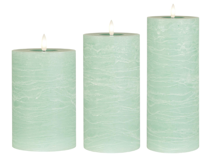 Tre lysegrønne bloklys i forskellige højder, alle tændt og arrangeret side om side mod en hvid baggrund.