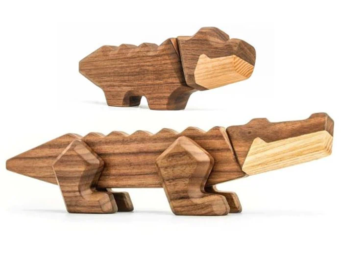 To trælegetøjsdyr, det ene ligner en dinosaur og det andet en krokodille, begge lavet af mørke og lyse træstykker, udstillet på en hvid baggrund.