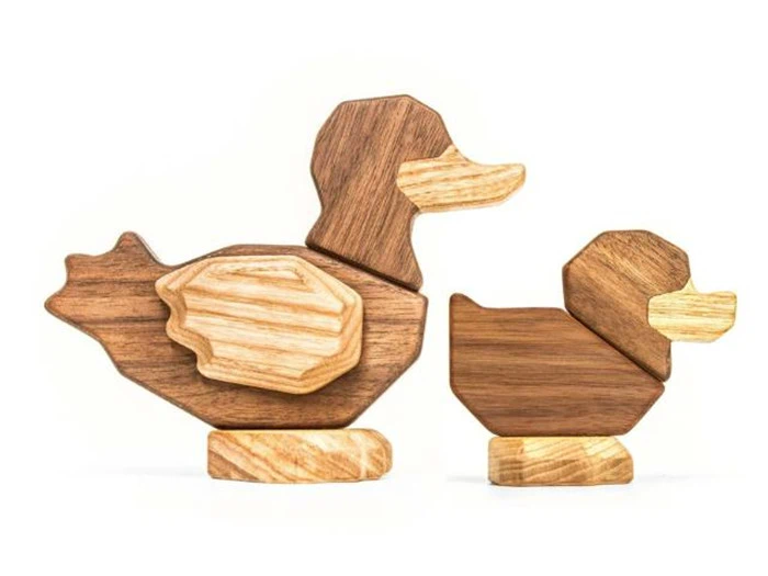 To legetøjsænder af træ, en større og en mindre, lavet af forskellige nuancer af træ, er placeret side om side på en hvid baggrund.