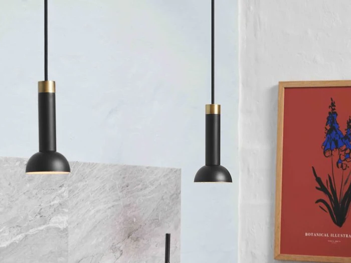 To moderne sorte pendler hænger fra loftet nær en væg med et botanisk print med rød ramme og lysegrå marmorfliser.