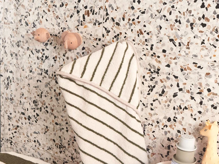 Et stribet håndklæde hænger på terrazzo-vægkroge formet som dyreansigter over toiletsager og en lille giraffigur.