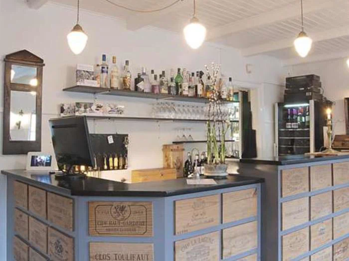 En hyggelig bar med en disk lavet af vinkasser i træ, hylder med flasker og glas og pendellamper, der hænger ned fra loftet.