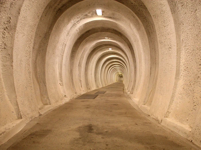 En lang, buet tunnel med jævnt fordelte, afrundede buer og ovenlys, alt sammen i et beige, betonlignende materiale.