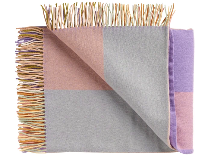 Foldet uldtæppe med rosa, grå og lavendelfarvede blokke og flerfarvede frynser langs kanterne, vist på en hvid baggrund.