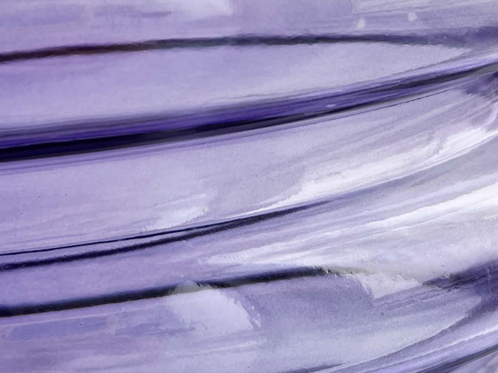 Nærbillede af hvirvlende lilla og hvid maling, der skaber lagdelte, buede mønstre med en blank tekstur.