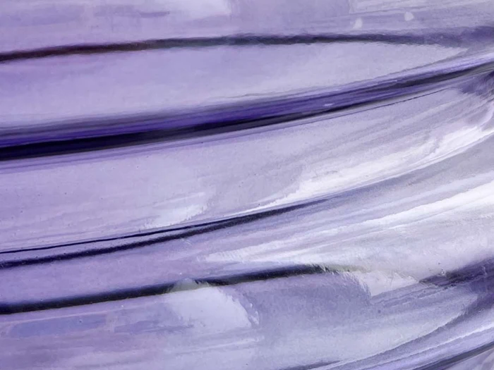 Nærbillede af hvirvlende lilla og hvid maling, der skaber lagdelte, buede mønstre med en blank tekstur.