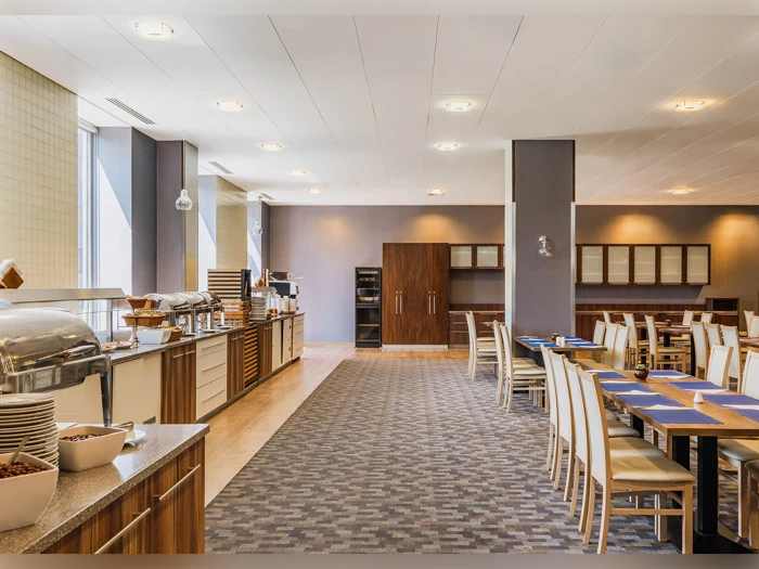 Et rummeligt, moderne spiseområde med træborde og -stole, en buffetdisk med overdækkede fade og god belysning.