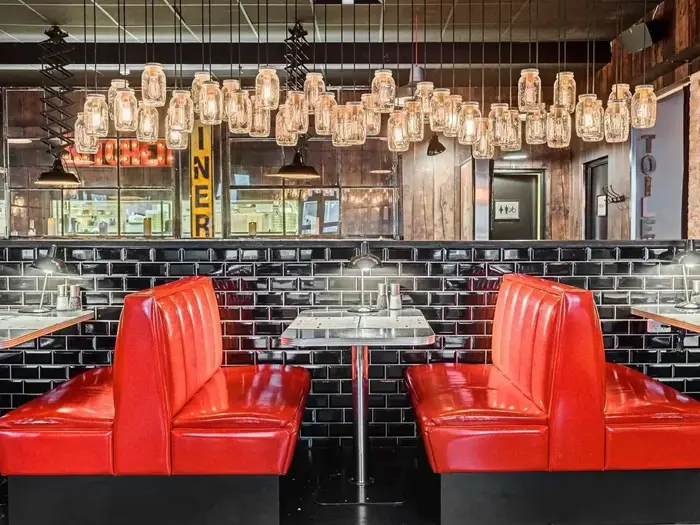 En retro diner-indretning med skinnende røde siddepladser, sorte kakkelvægge og murerbalje-pendler, der hænger over borde med marmortop.