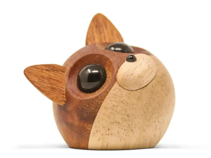 En lille, rund træfigur af en kat med store sorte øjne, opretstående ører og et skråt hoved, fremstillet af træ i forskellige nuancer.