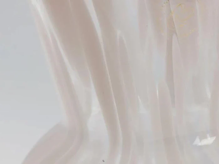 Et nærbillede af en gennemskinnelig, bølget overflade med bløde hvide og beige toner, der skaber et abstrakt, flydende mønster.