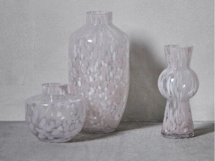 Tre gennemskinnelige glasvaser med et spættet hvidt mønster står på en grå overflade mod en lysegrå baggrund.