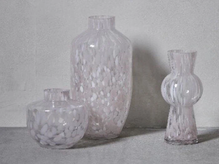 Tre gennemskinnelige, mønstrede glasvaser i forskellige former og størrelser er arrangeret på en lysegrå flade mod en lys væg.