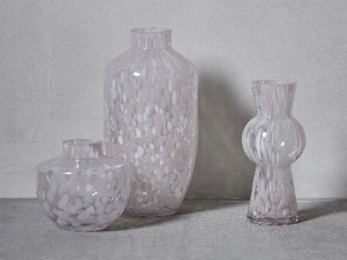 Tre gennemskinnelige glasvaser med hvidplettede mønstre er arrangeret på en grå overflade mod en lysegrå baggrund.