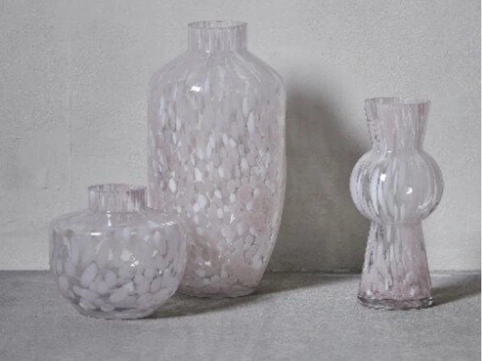 Tre gennemskinnelige glasvaser med hvidplettede mønstre er arrangeret på en lysegrå overflade mod en ensfarvet baggrund.