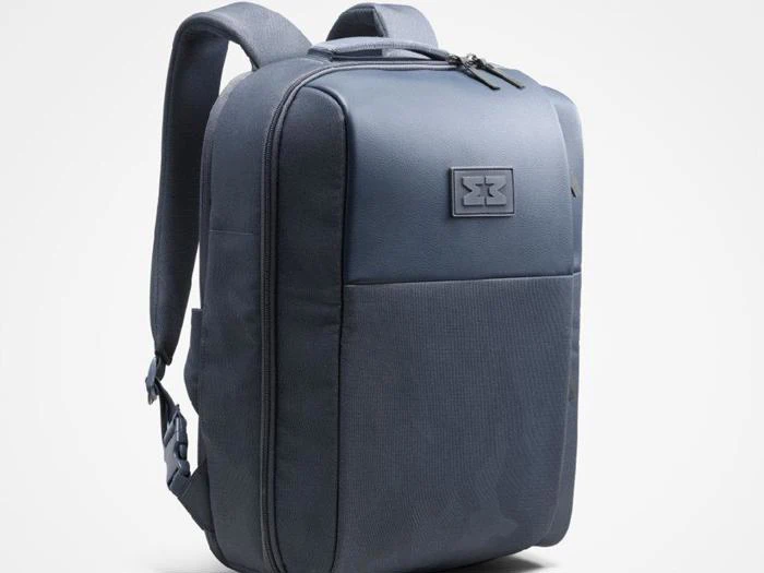 En elegant, blå rygsæk med polstrede skulderstropper, en forlomme, lynlås i toppen og et rektangulært logopatch på forsiden.