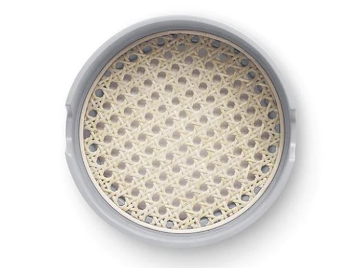 En rund, flettet overflade af spanskrør eller rattan i en hvid, cirkulær ramme, som ligner sædet på en traditionel stol, set ovenfra.