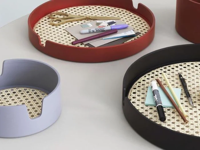 Runde bakker med vævet bund i rød, sort og lavendel indeholder papirvarer som kuglepenne, sakse og notesblokke, der er arrangeret på en lys overflade.