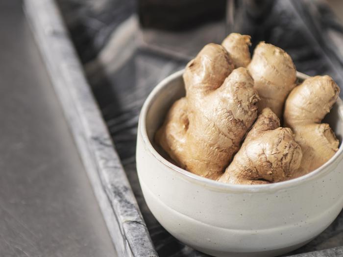 En hvid keramikskål fyldt med frisk ingefærrod står på en marmorbakke.