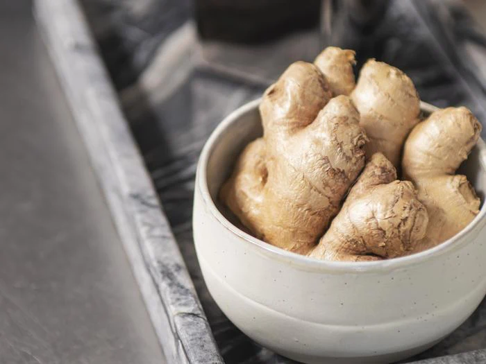 En hvid keramikskål fyldt med frisk ingefærrod står på en marmorbakke.