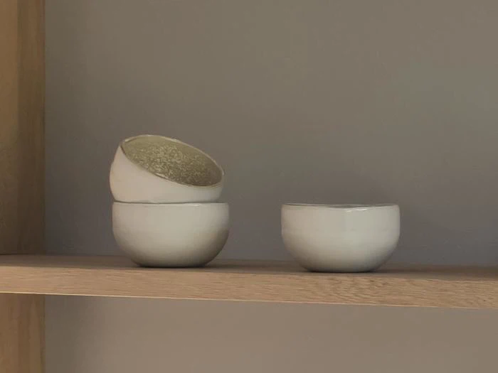 Tre små hvide keramikskåle på en træhylde; to er stablet med den øverste på skrå, og en skål står for sig selv.