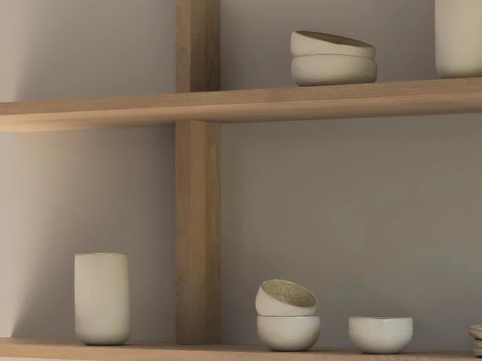 Minimalistiske træhylder med enkle, håndlavede hvide keramiske kopper og skåle, med dæmpet belysning og en neutral væg i baggrunden.