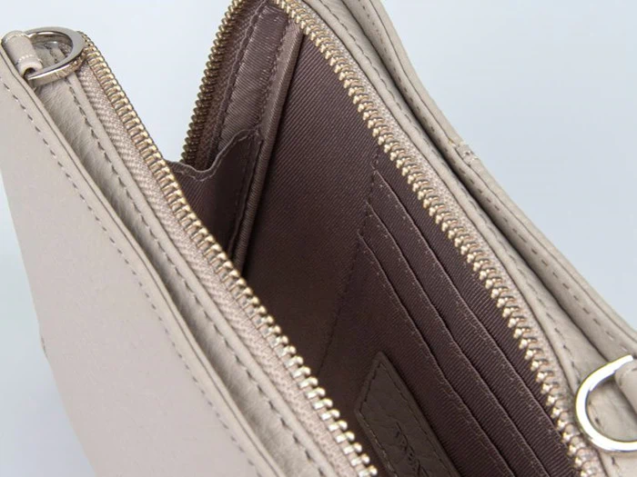 Nærbillede af en åben beige pung med lynlås, der viser indvendige rum og kortlommer foret med brunt stof.