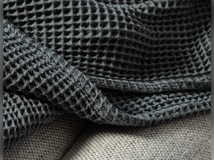 Et nærbillede af et mørkegråt stof med vaffelstruktur, der er draperet over en lysere overflade med glat struktur.