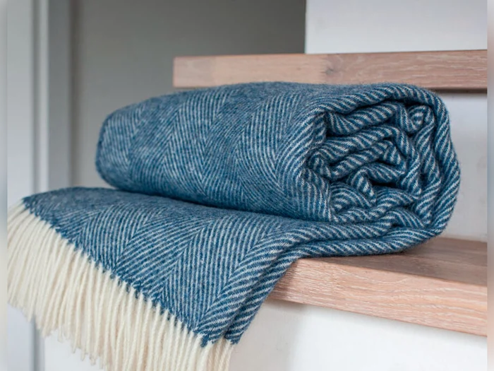 Et foldet blåt sildebensmønstret tæppe med hvide frynser er placeret på en træhylde.