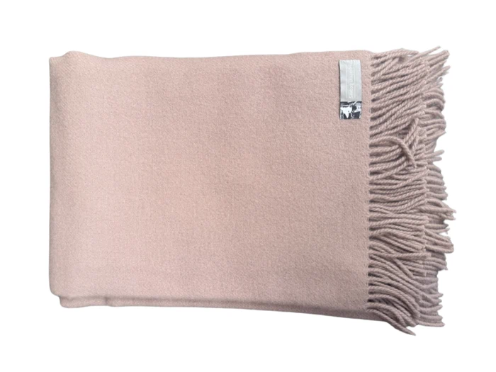 Et foldet lyserødt tæppe med frynsede kanter på den ene side og et lille skinnende mærke nær frynsen.