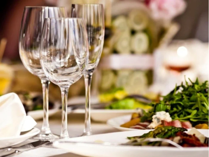 Et nærbillede af et bord med tomme vinglas, hvide servietter og tallerkener med frisk salat, med en let sløret baggrund, der antyder en formel spisesituation.