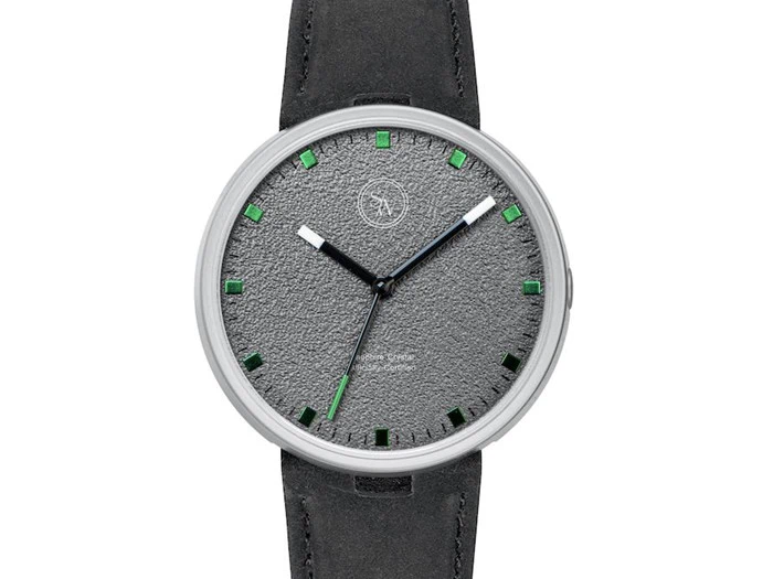 Et minimalistisk armbåndsur med en struktureret grå urskive, grønne timemarkeringer, sort rem og sølvfarvet ramme. Urets visere er sorte med en grøn sekundviser.