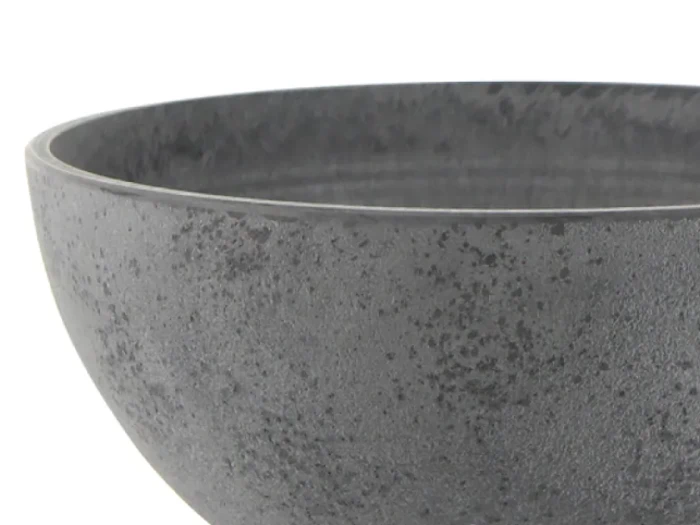 Nærbillede af en struktureret, mørkegrå keramikskål mod en hvid baggrund. Kun en del af skålen er synlig.