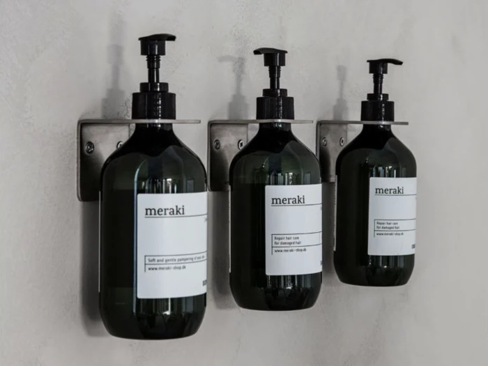 Tre vægmonterede sorte pumpeflasker mærket meraki står på rad og række på en lys væg.