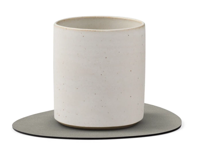 En almindelig, hvid keramikkop med diskrete pletter, placeret på en flad, uregelmæssigt formet grå bordskåner mod en hvid baggrund.