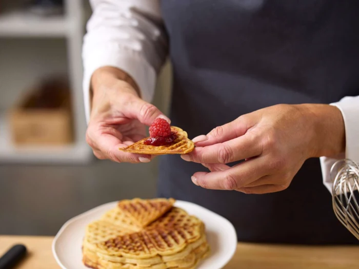 En person, der lægger et hindbær på en vaffel.