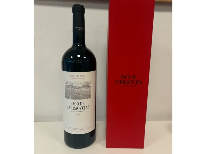 En flaske Pago de Carraovejas-rødvin står ved siden af en høj, rød kasse med samme etiket på en hvid flade.