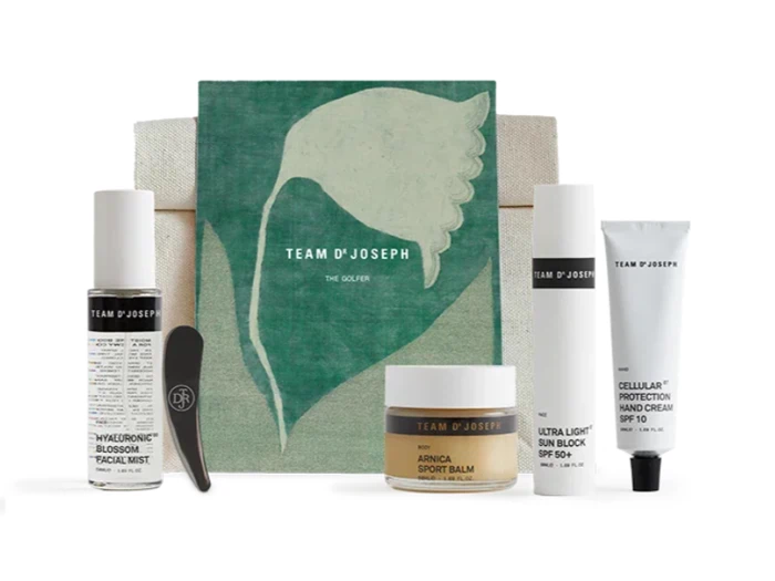 Et sæt med fem TEAM DR JOSEPH-hudplejeprodukter arrangeret foran en grøn pose med et hvidt bladdesign. Produkterne omfatter mist, balm, solcreme, håndcreme og et lille sort værktøj.