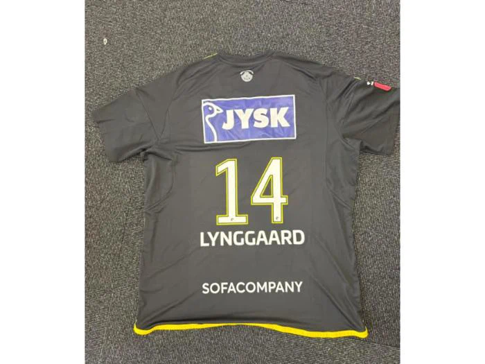 En sort sportstrøje med gule kanter, hvor der på ryggen står navnet LYNGGAARD, nummer 14 og sponsorerne JYSK og SOFACOMPANY, lå fladt på et tæppebelagt gulv.