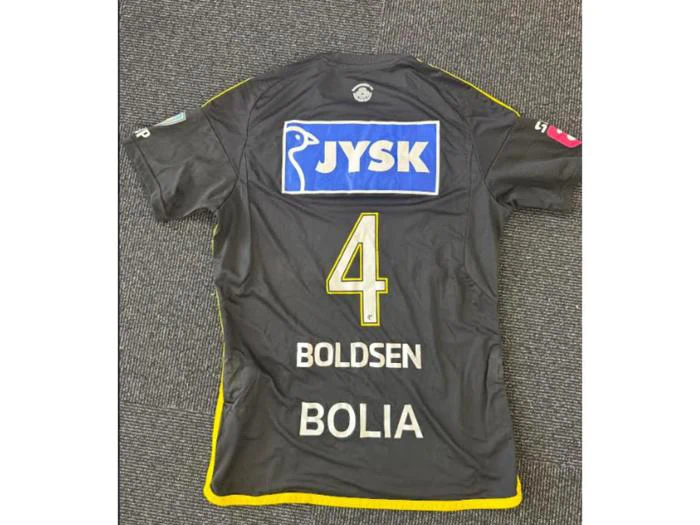 En sort sportstrøje med gule kanter, nummer 4, navnene Boldsen og Bolia samt et JYSK-sponsorlogo på ryggen lå på et gråt tæppe.