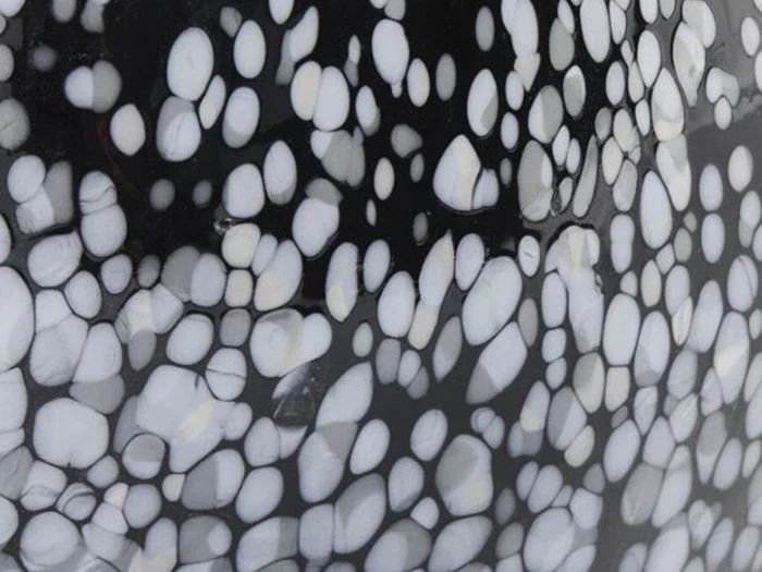 Nærbillede af en sort overflade med uregelmæssige hvide ovale og runde pletter, der ligner småsten eller et plettet dyremønster.
