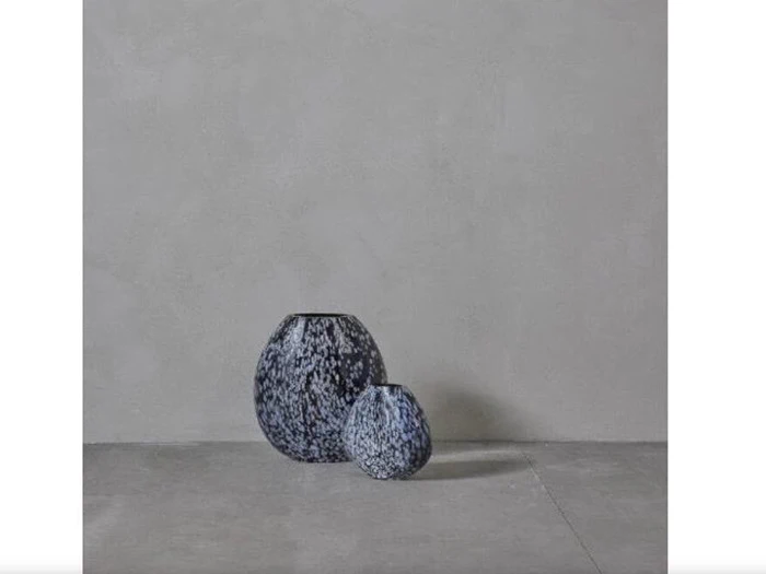 To runde, blåplettede vaser i forskellige størrelser står på et gråt betongulv mod en almindelig grå vægbaggrund.
