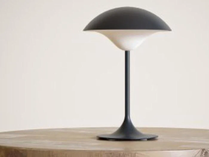 En moderne sort-hvid bordlampe med en kuppelformet skærm sidder på en rund træflade mod en ensfarvet lys baggrund.
