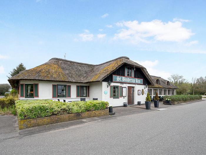 En hvid bygning med stråtag, grønne kanter og et skilt med teksten St. Andrew Inn ligger ved siden af en vej på en klar dag. Buske og potteplanter står langs facaden.