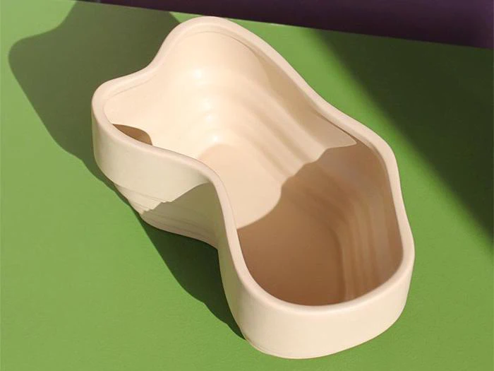 En beige, nyreformet plastikbalje står på en lysegrøn overflade, og sollyset kaster skygger hen over scenen.